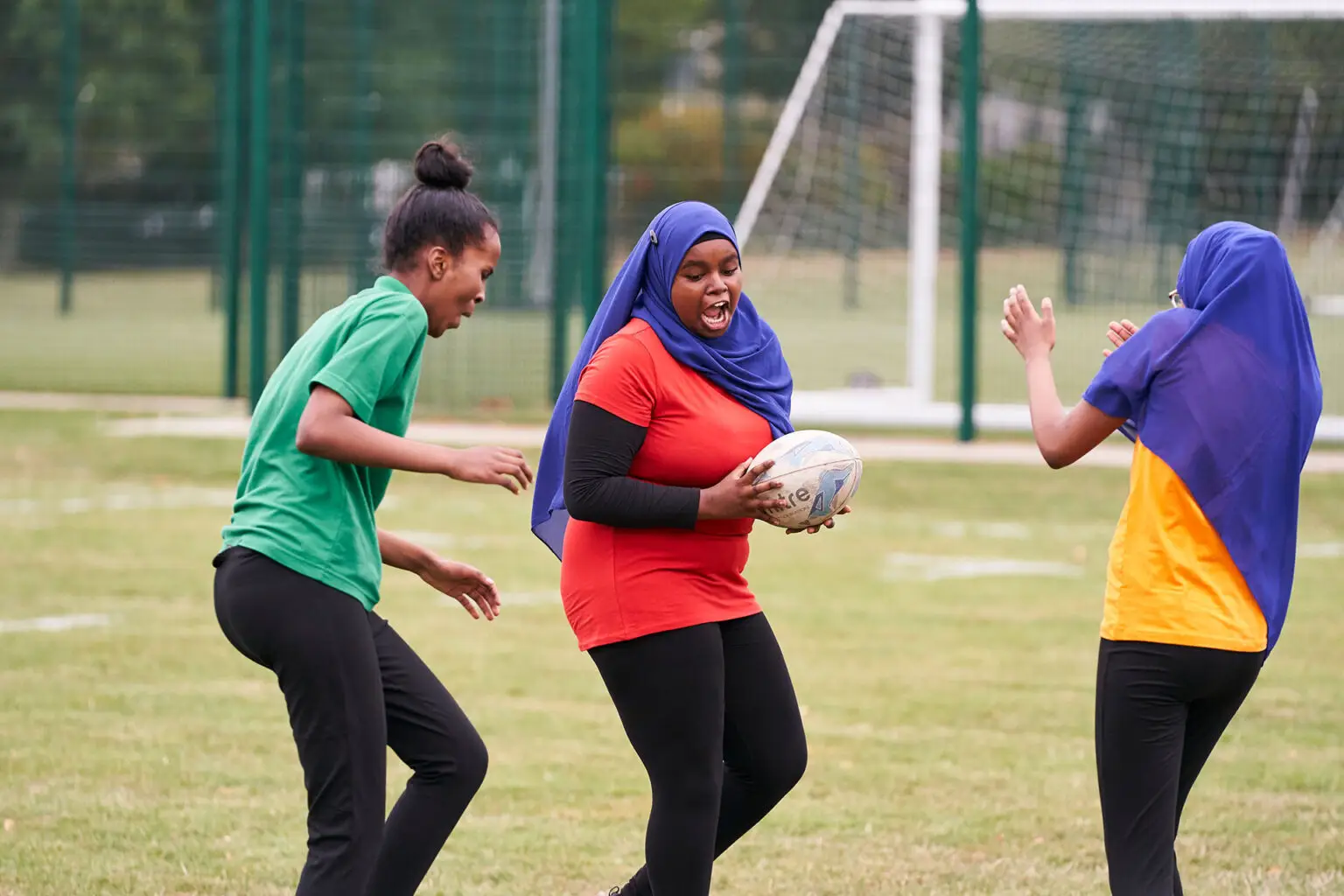 A group of girls, two of whom are wearing hijabs, playing rugby