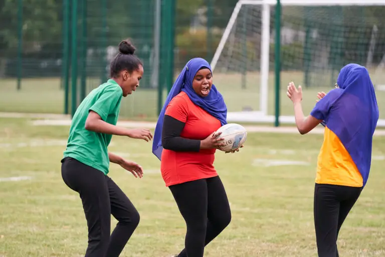 A group of girls, two of whom are wearing hijabs, playing rugby