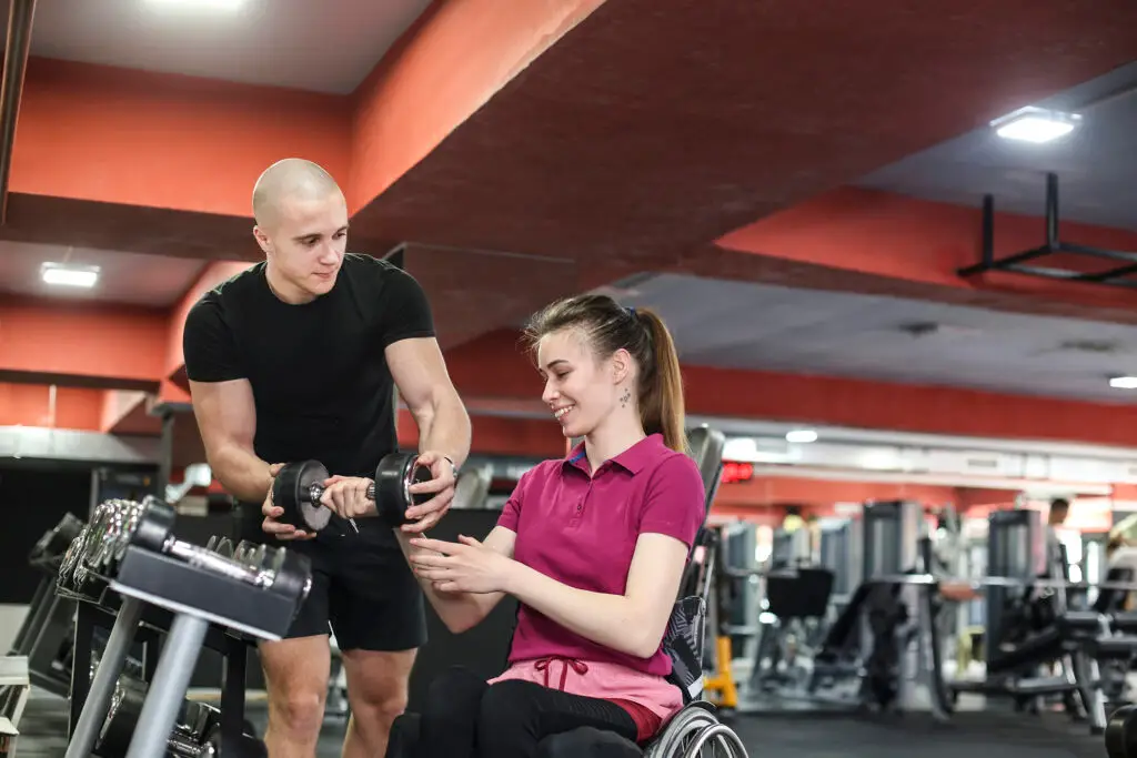 Disabled young woman exercising in a gym with help of her coach