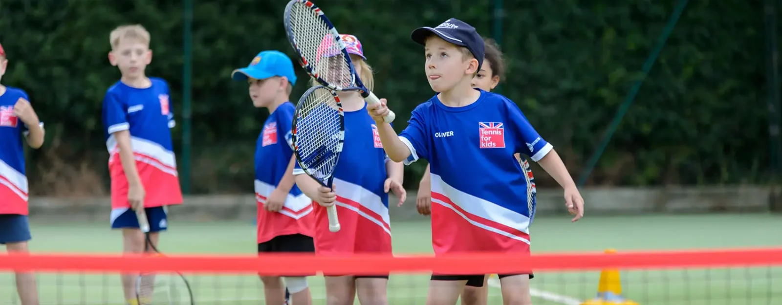 A group of children playing tennis wearing 'Tennis for kids' t-shirts