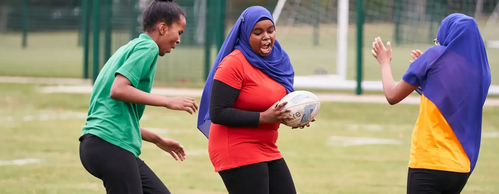A group of girls, two of whom are wearing hijabs, playing rugby
