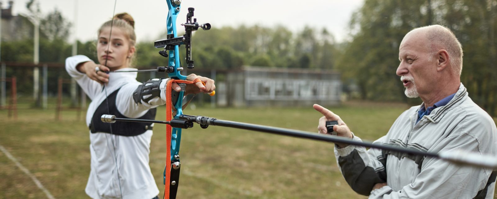 Archery Training A coach working with an archer on their form as they aim an arrow