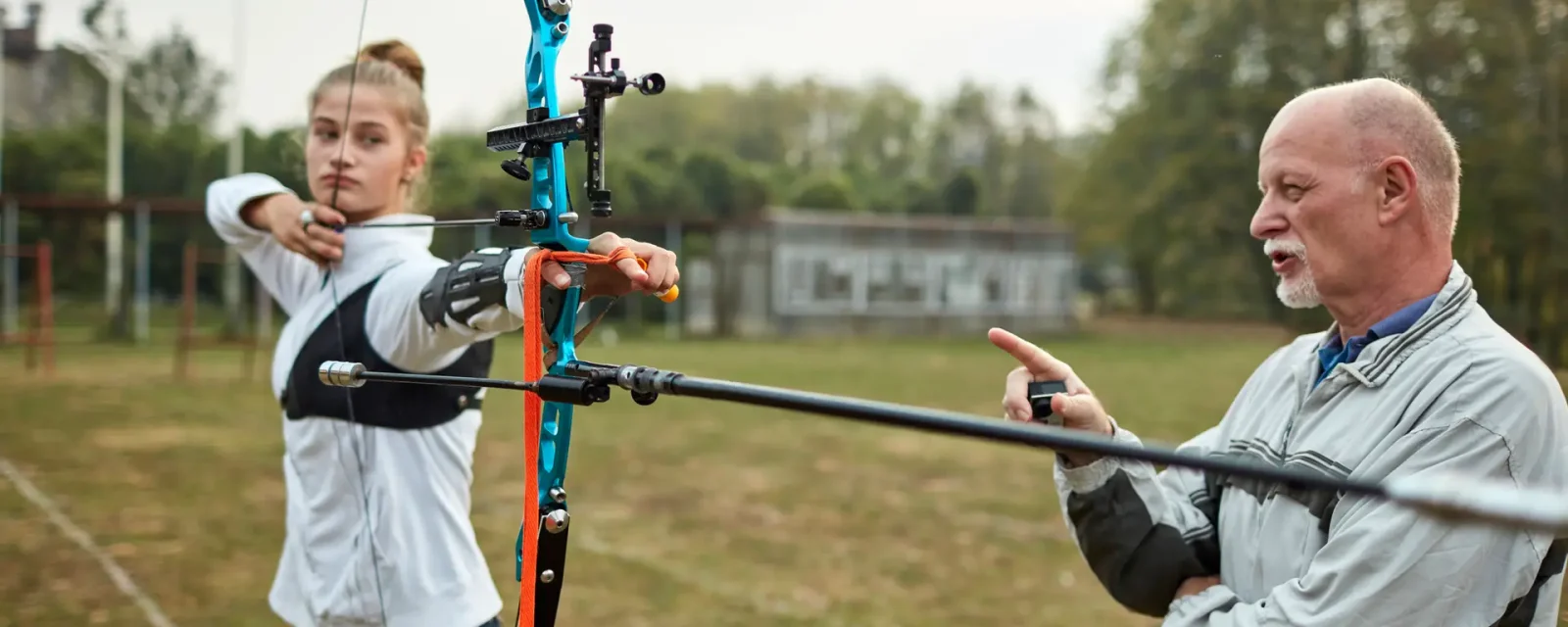 A coach working with an archer on their form as they aim an arrow