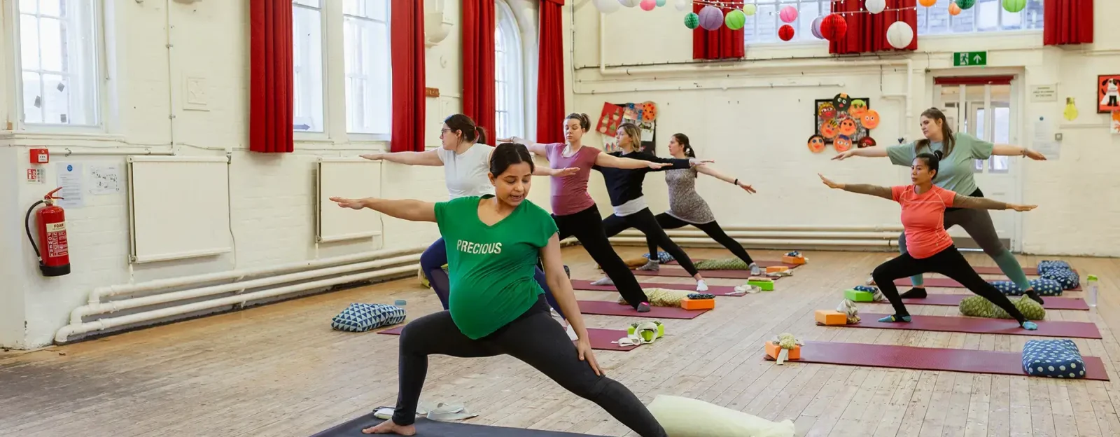 Asian and Indian ethnicity business lady, teaching a heavily pregnant yoga class warrior pose