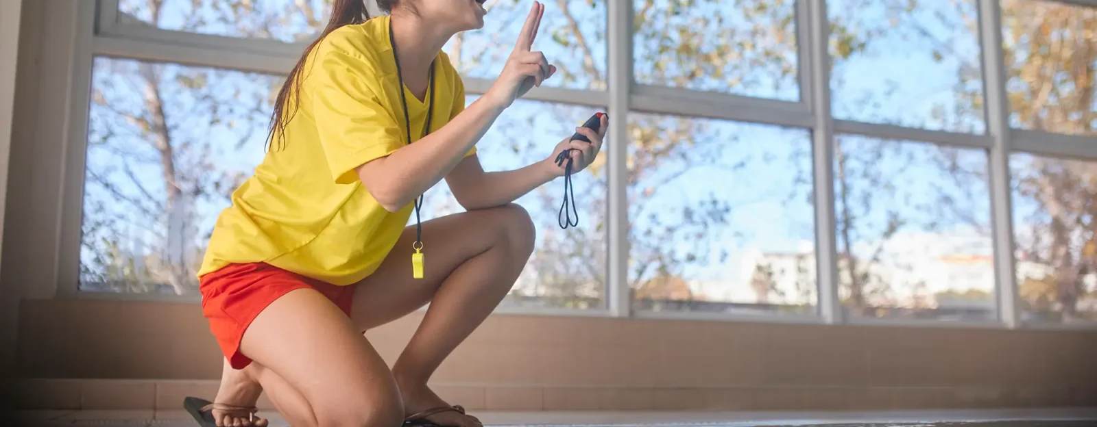 Female lifeguard holding timer giving instructions to swimmers in indoor pool