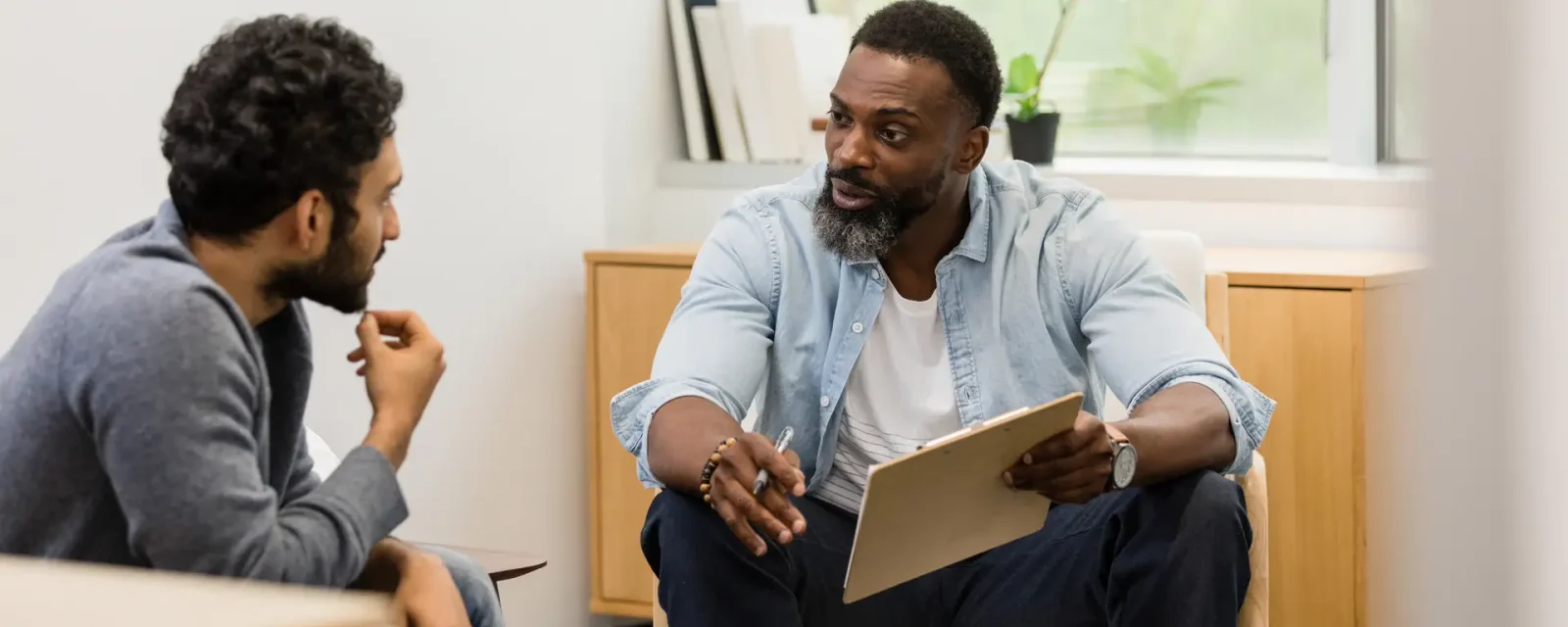 Male counselor asks young adult man questions Two men talking to each other in a small room.