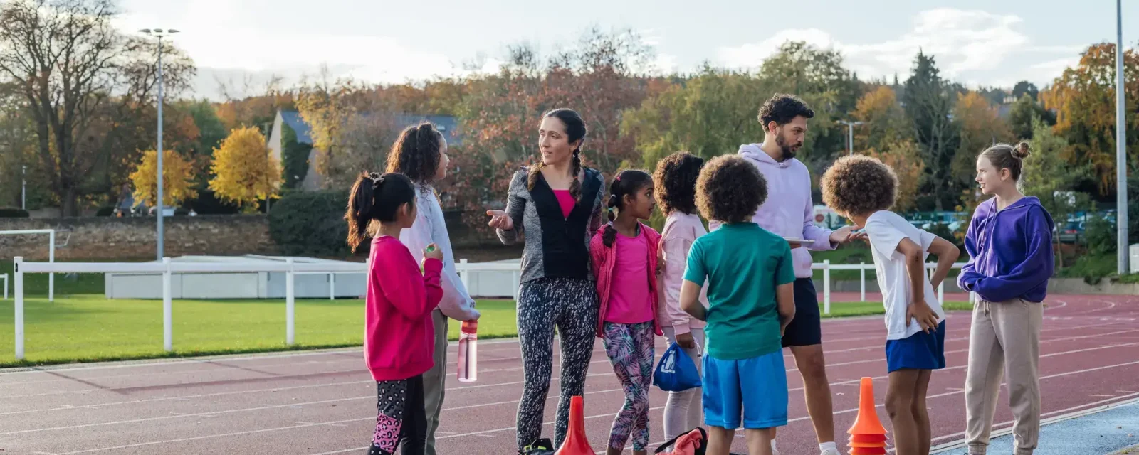 A group of children and two coaches talking together by an athletics track outside Wentworth Leisure Centre in Hexham, North East England.