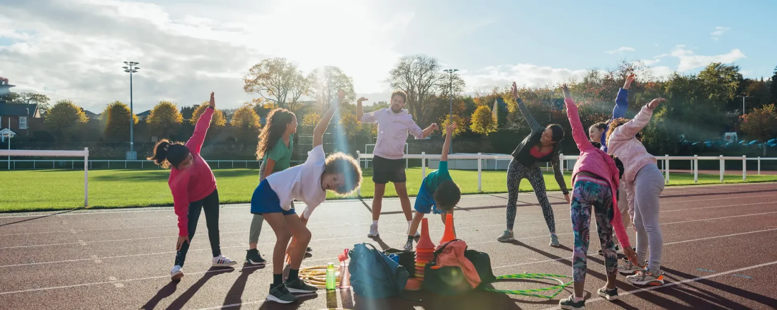 A group of children and two coaches stretching together by an athletics track outside Wentworth Leisure Centre in Hexham, North East England.