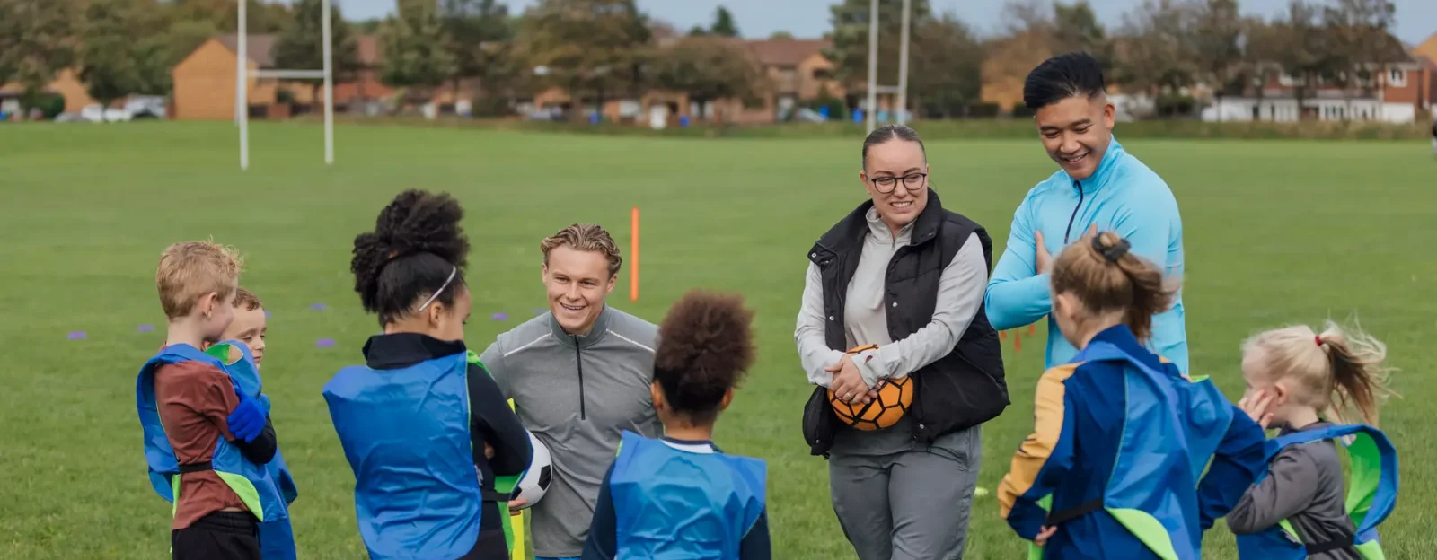Coaches teaching a group of under 10's football on a pitch.