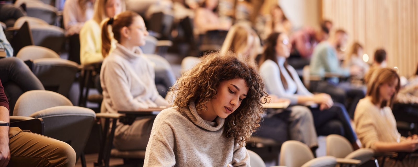 Writing an exam at the university A group of students writing notes in a lecture hall