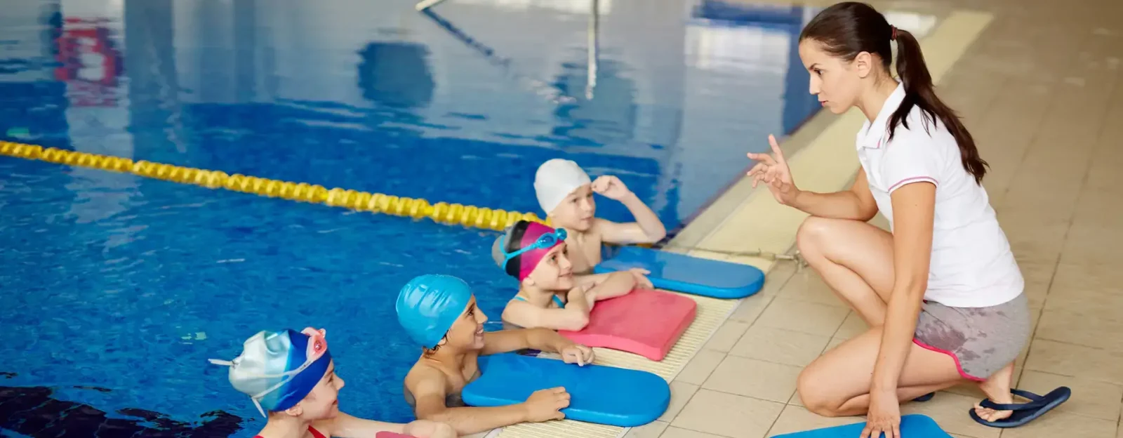 Children in pool listening to swimming instructor at side of pool.