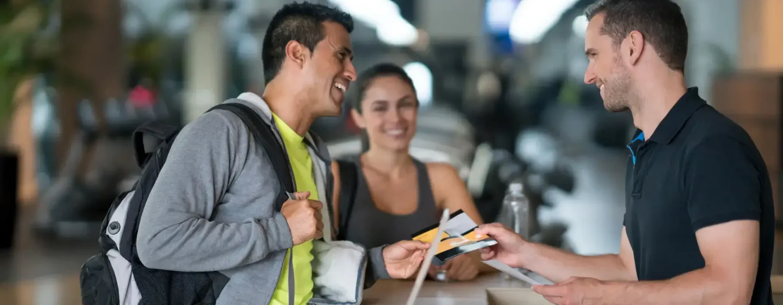 Two people speaking to a receptionist at their gym and receiving a flyer