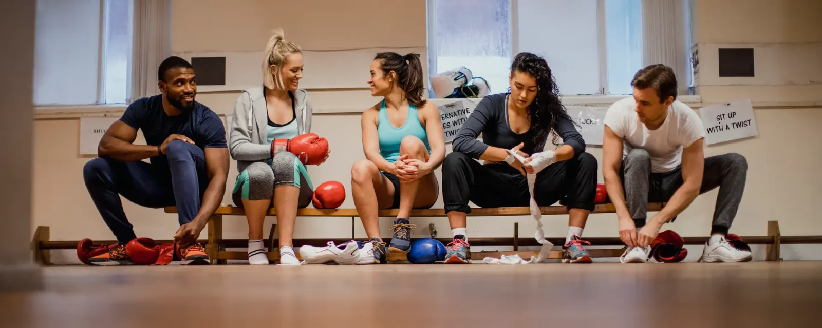 Athletes Sitting On a Bench in a Boxing Gym A group preparing for an exercise class in a gym wrapping their hands with bandages before boxing training.