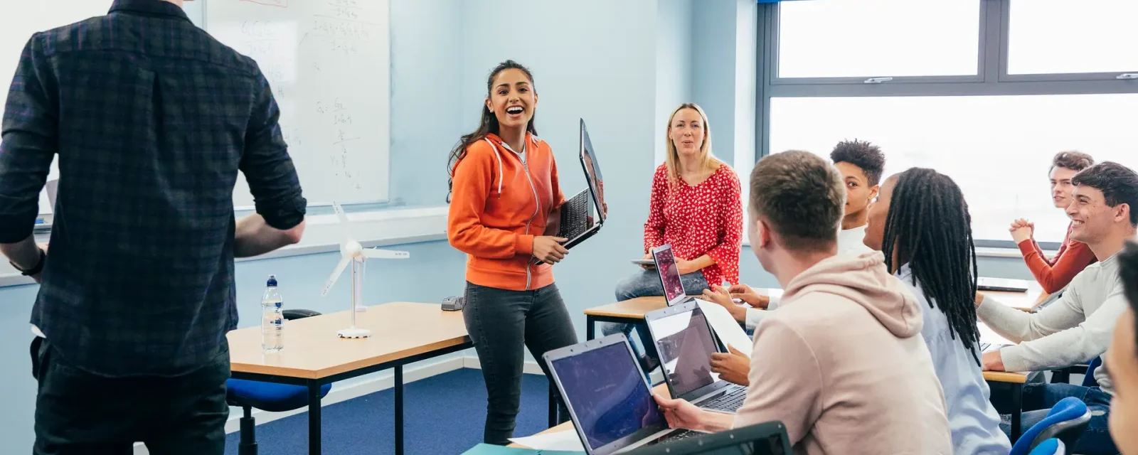 A group of students working in a classroom with one student presenting to the group.
