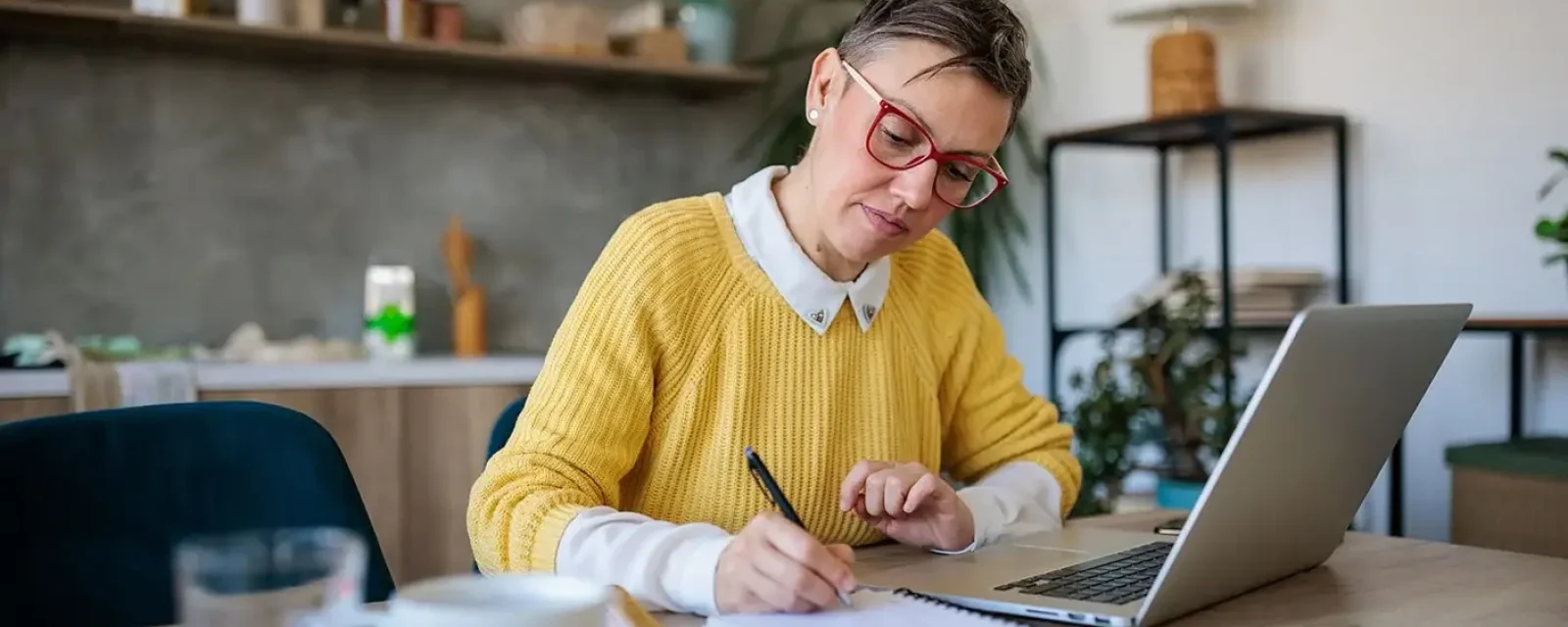 A person working at a laptop and writing in their notebook at home